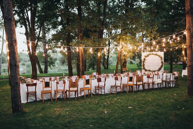 Festive table served dishes and decorated with branches of greenery, stands on green grass in the area of wedding party. What to charge for event planning services article.