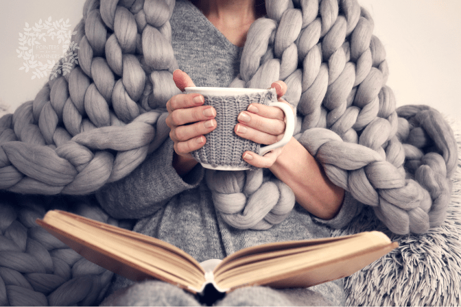 woman cozied under blanket with a mug and a book