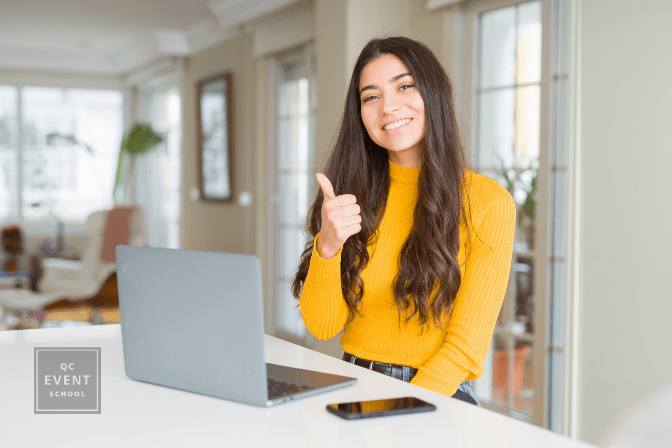 Young woman using computer laptop doing happy thumbs up gesture with hand. Approving expression looking at the camera with showing success.