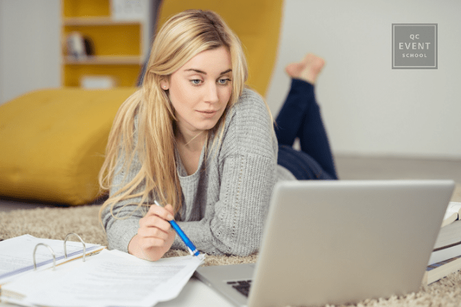 woman lying on floor with binder and laptop, doing schoolwork from home