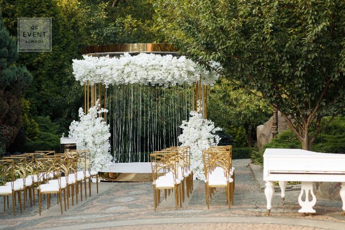 Luxurious yellow-gold wedding arch decorated with white flowers in nature among the trees. wedding ceremony. white piano on the nature. chairs for guests on the street.