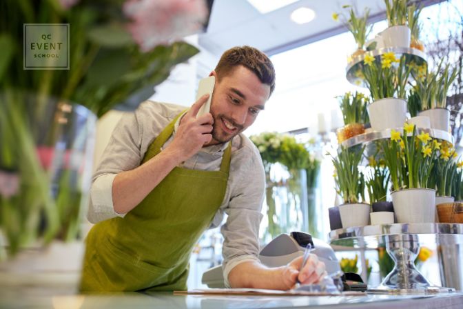 people, sale, retail, business and floristry concept - happy smiling florist man calling on smartphone and making notes to clipboard at flower shop counter