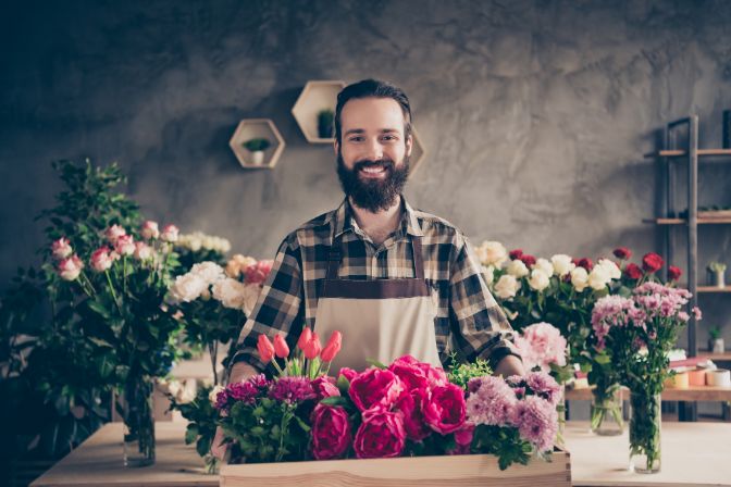 Portrait of his he nice attractive cheery cheerful content guy professional company founder enjoying holding big large box peony tulip diverse at industrial loft concrete style indoors