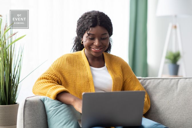 Smiling young black woman in knitted sweater freelancer working from home, sitting on couch, using laptop, copy space. Relaxed african american lady enjoying her weekend, surfing on internet on laptop