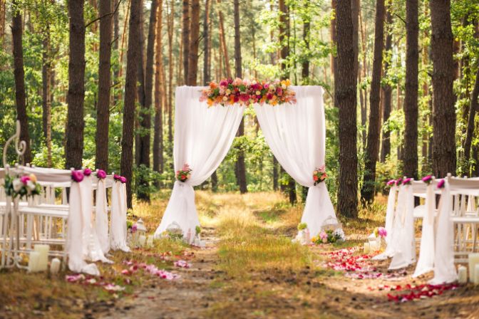 Beautiful romantic festive place made with wooden square and floral roses decorations for outside wedding ceremony in green park. Wedding settings at scenic place. Horizontal color photography. Fall wedding trends.