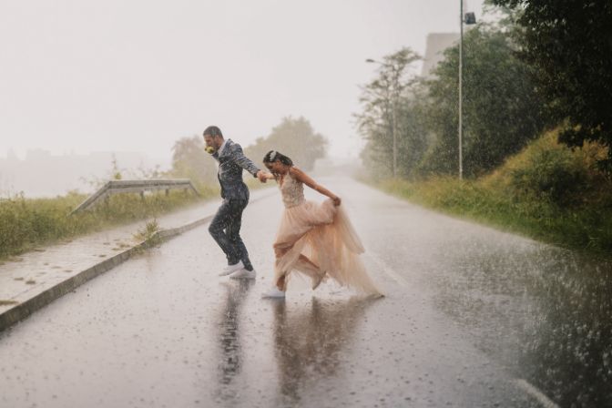 Silly young just married couple crossing road on rainy day. Running in wet ceremonial clothes. Problem-solving event planners article.