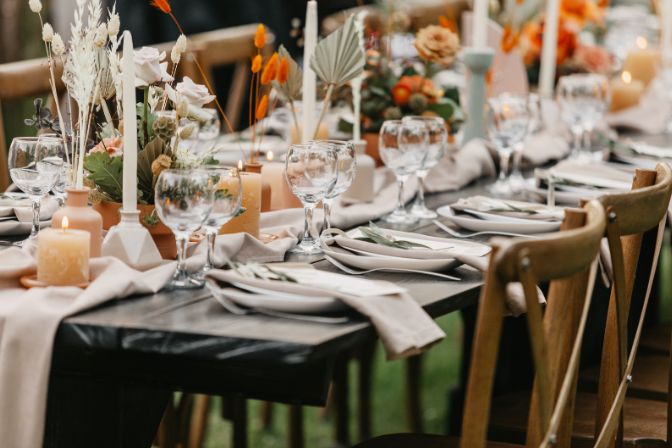 Event and catering agency organization modern wedding in boho style. Table for guests assembled with dishes, cutlery, glasses and flowers, candles and elements, chairs on green lawn, flat lay, outdoor. Event decorating article.