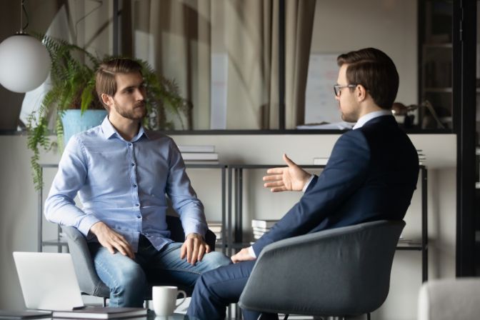 Colleagues businessmen discussing project strategy, sharing ideas, sitting in armchairs in modern office, business partners negotiating startup, hr manager holding interview with candidate. Difficult clients article.